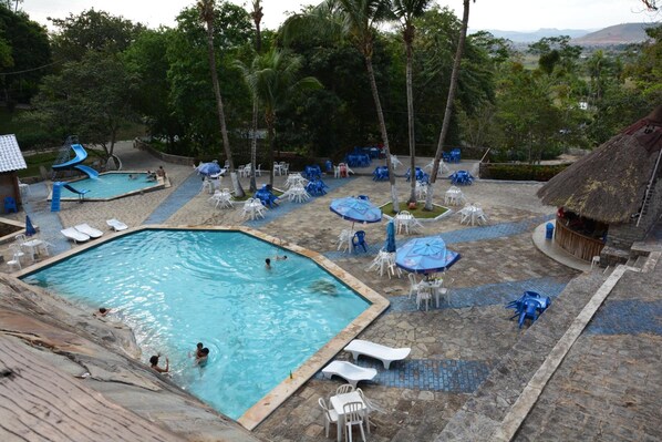 Un área de piscina con varias piscinas, sillas de descanso y sombrillas.