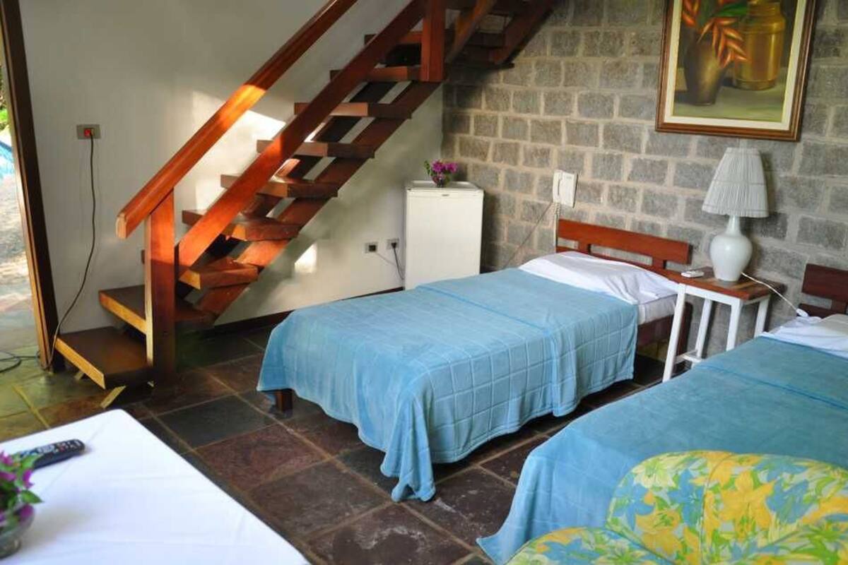 A room with two beds, a wooden staircase, a small white cabinet, and a painting on the wall.
