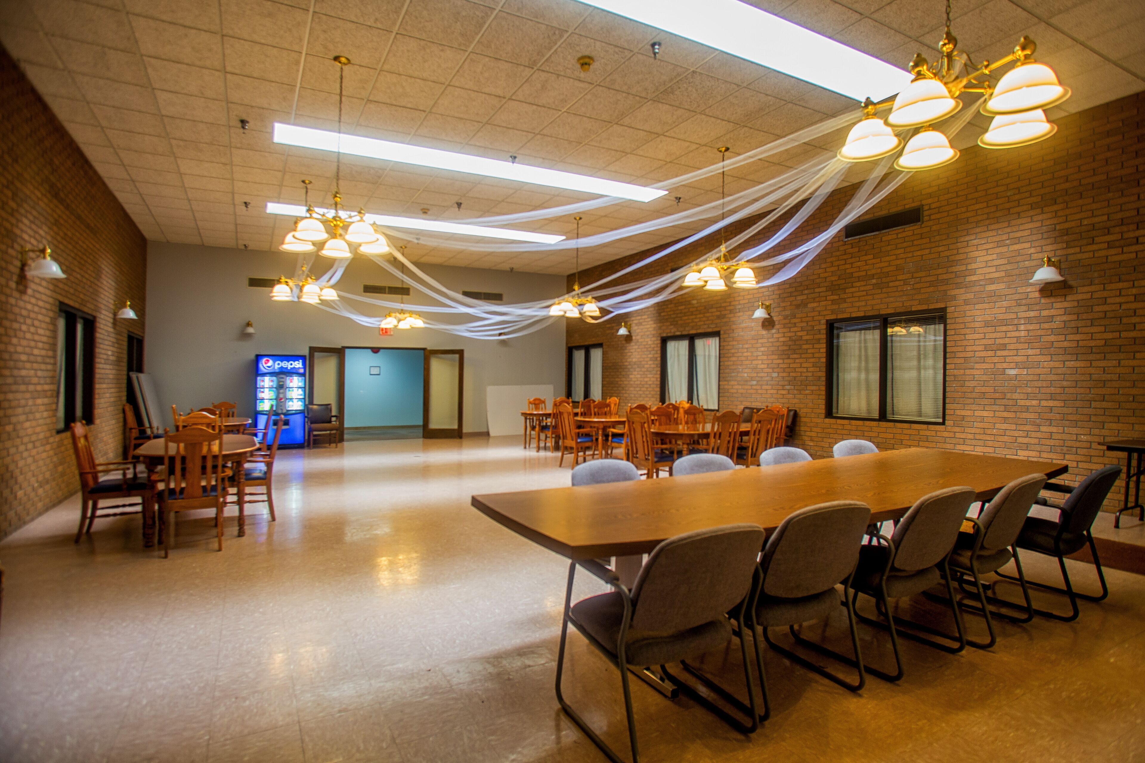 A conference room with a long table, multiple chairs, and hanging lights.
