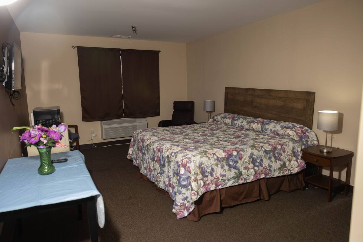 A hotel room with a bed, a desk, a chair, a lamp, and a vase with flowers.