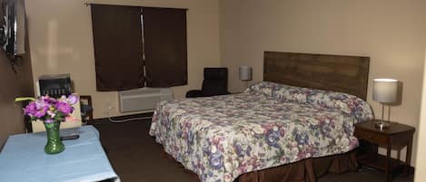 Habitación de hotel con cama, escritorio, silla, lámpara y un florero con flores.