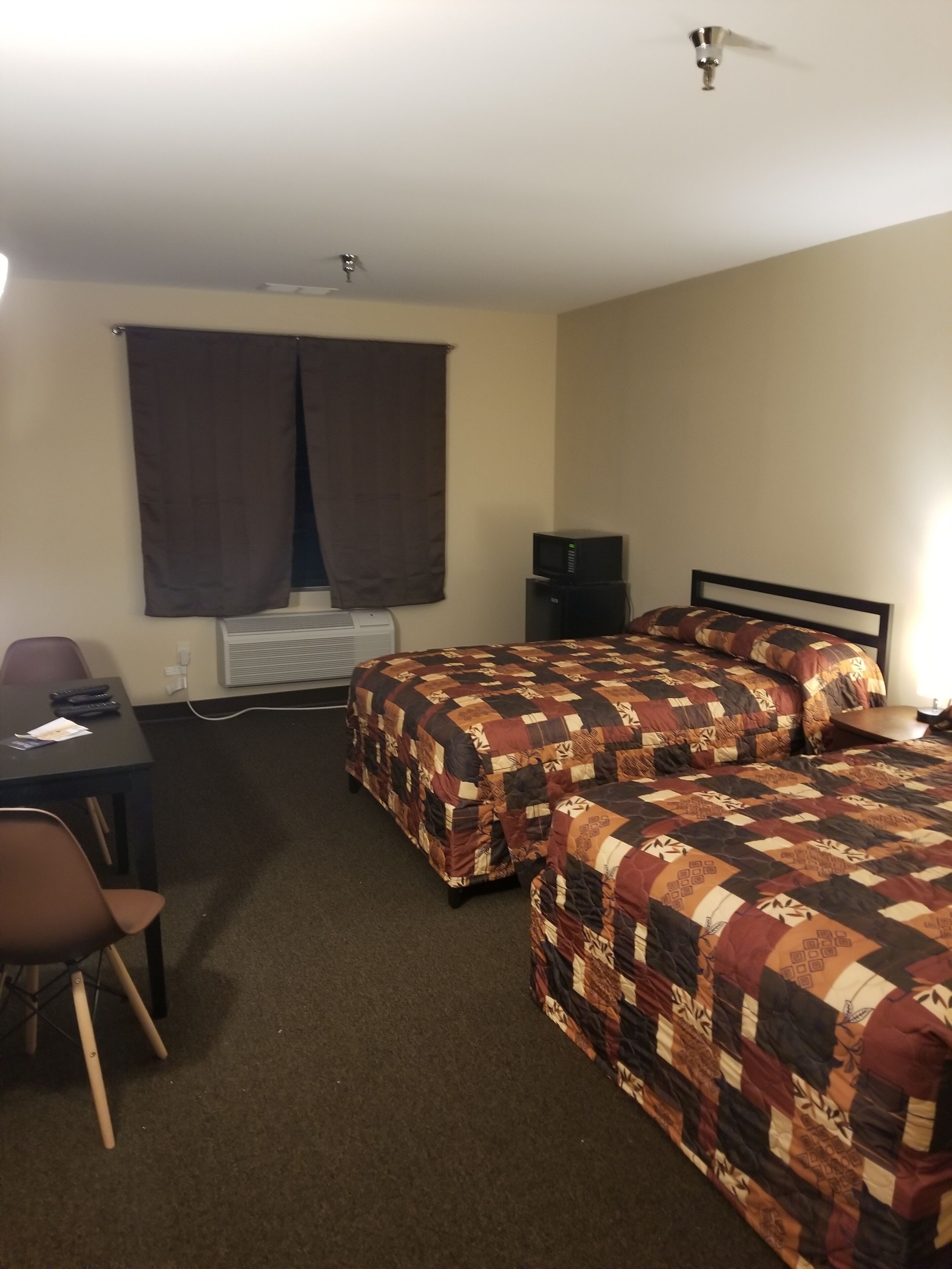 Habitación de hotel con dos camas, un escritorio, una silla, un televisor y una ventana con cortinas.