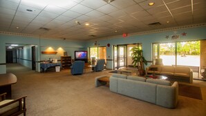 A spacious lobby with a large blue sofa, a television, and a coffee table. There are several chairs and a small table with items on it. - Lafayette Inn (Moundsville)