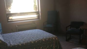 A room with two beds, a chair, a desk, and a window with blinds.