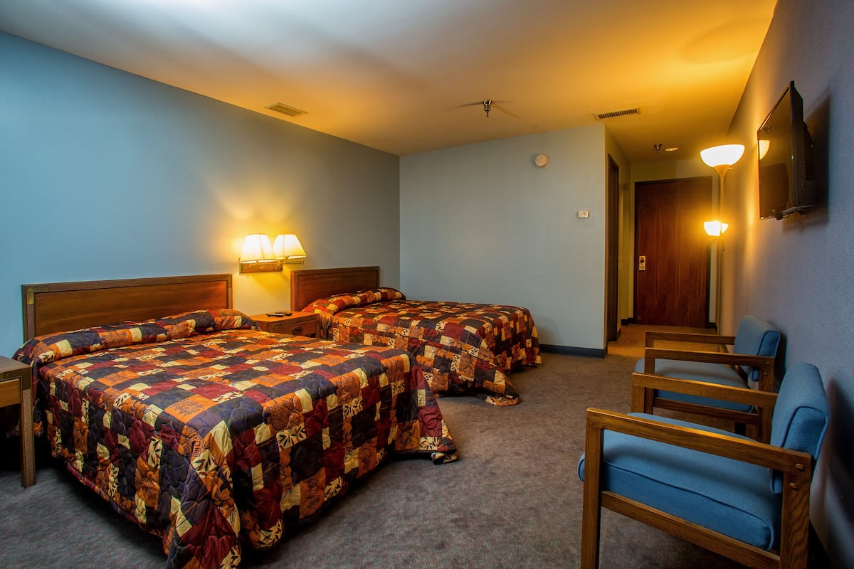 A hotel room with two beds, a desk, a chair, and a TV on the wall.
