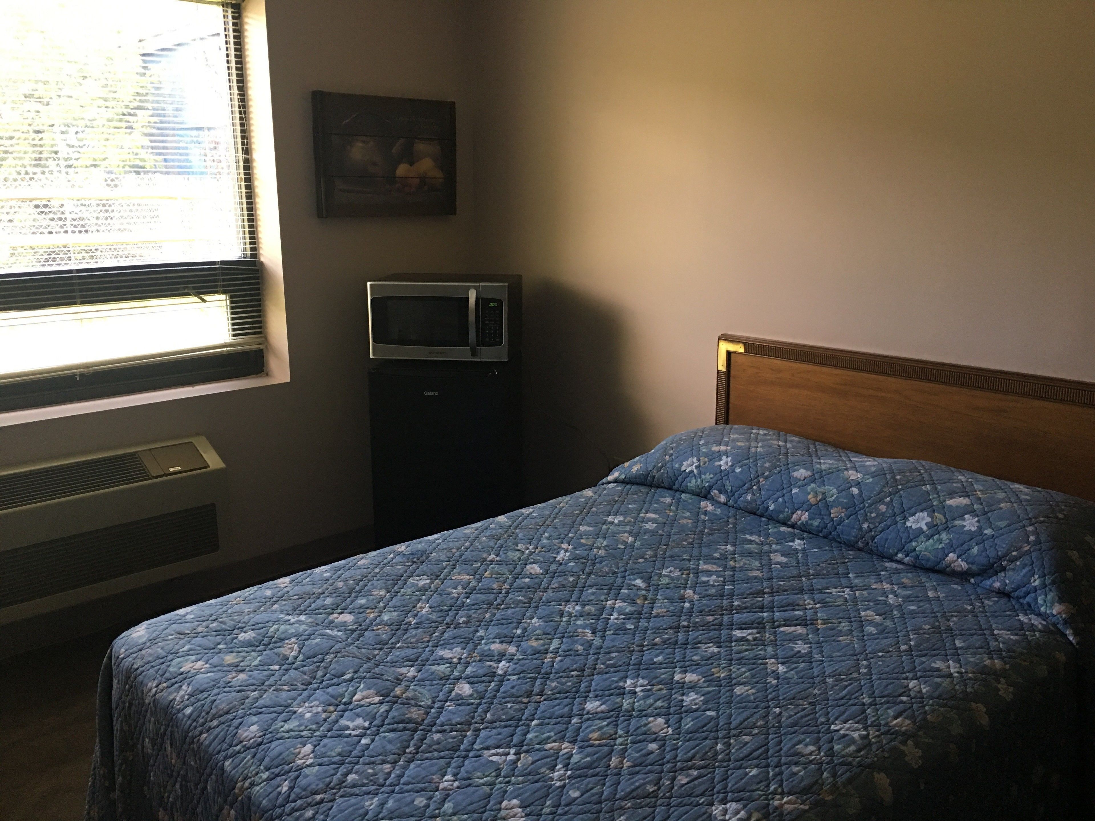 A bedroom with a bed, a wall-mounted TV, a heater, and a window with blinds.