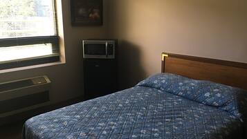 A bedroom with a bed, a wall-mounted TV, a heater, and a window with blinds.