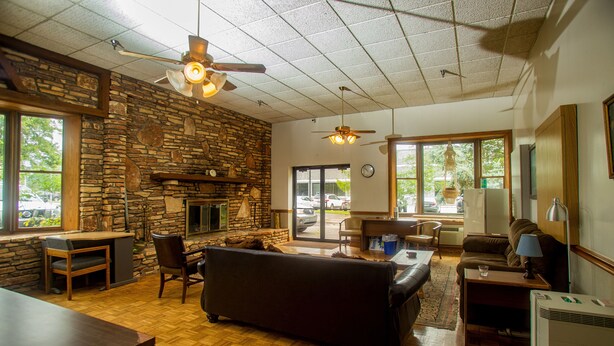 A spacious living area with a stone wall, a fireplace, a ceiling fan, and large windows. - Lafayette Inn (Moundsville)