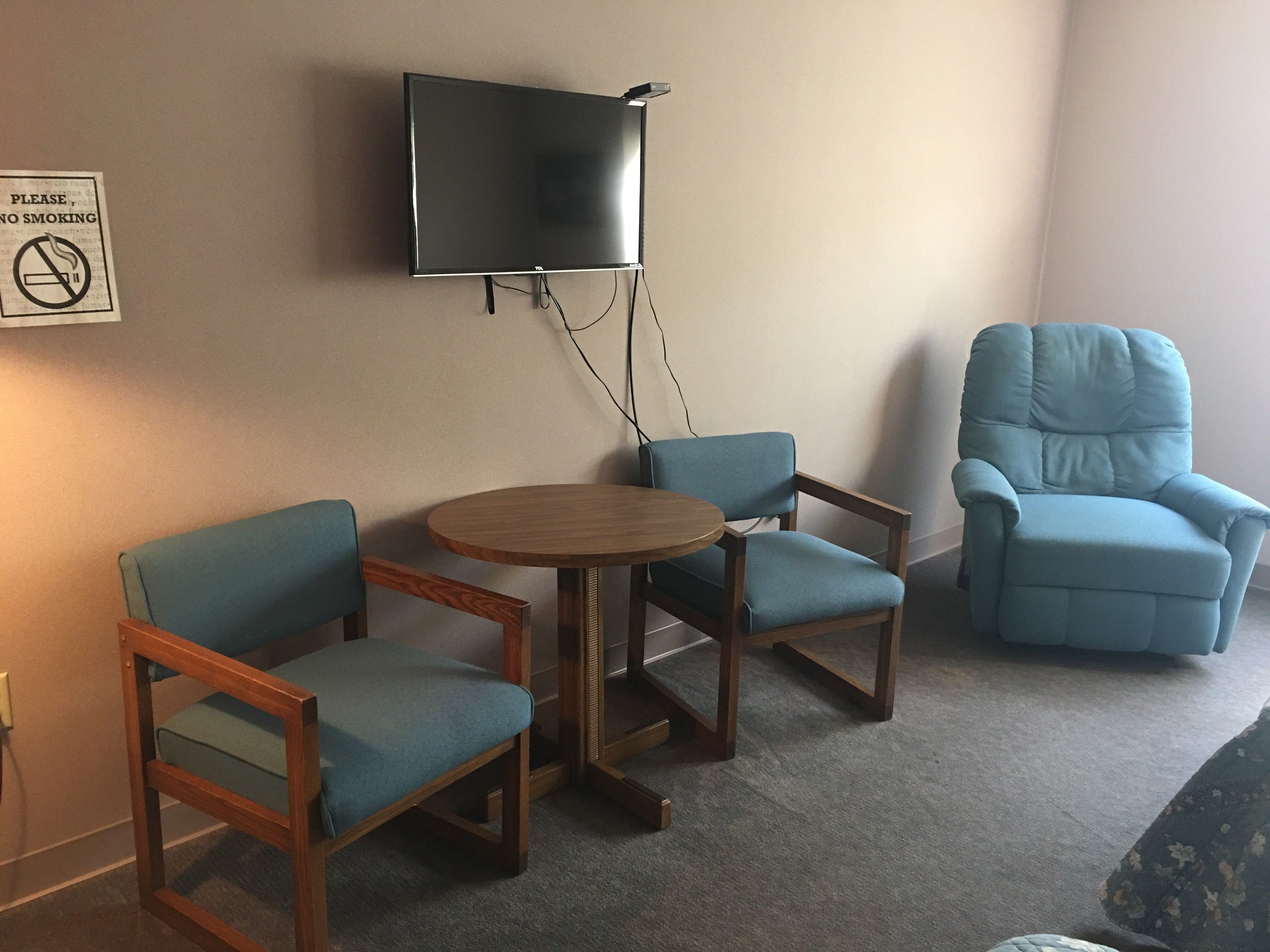 Una habitación con dos sillones azules, una mesa de madera y un televisor montado en la pared.
