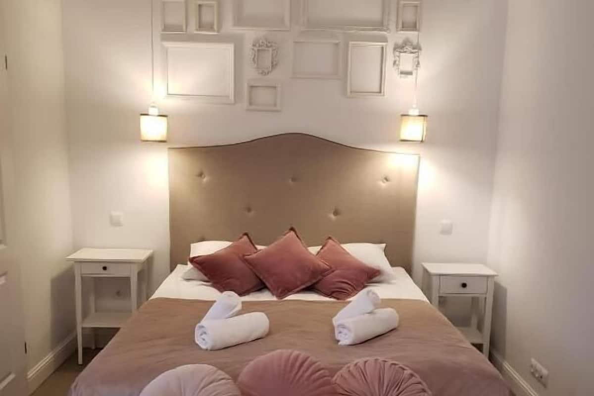 Ein ordentlich bezogenes Bett mit einer gebürsteten Kopfstütze, zwei Nachttischen und einer Bank am Fußende.