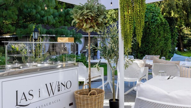 An outdoor seating area with white wicker furniture, a buffet station labeled "LAS i WNO," and greenery in the background. - Dwór Konstancin (Konstancin-Jeziorna)