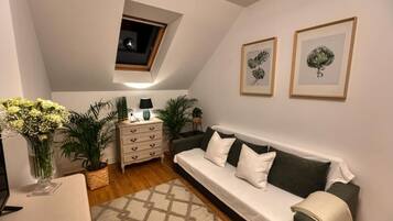 A cozy living room with a sofa, a small table, a lamp, and two framed botanical prints on the wall.