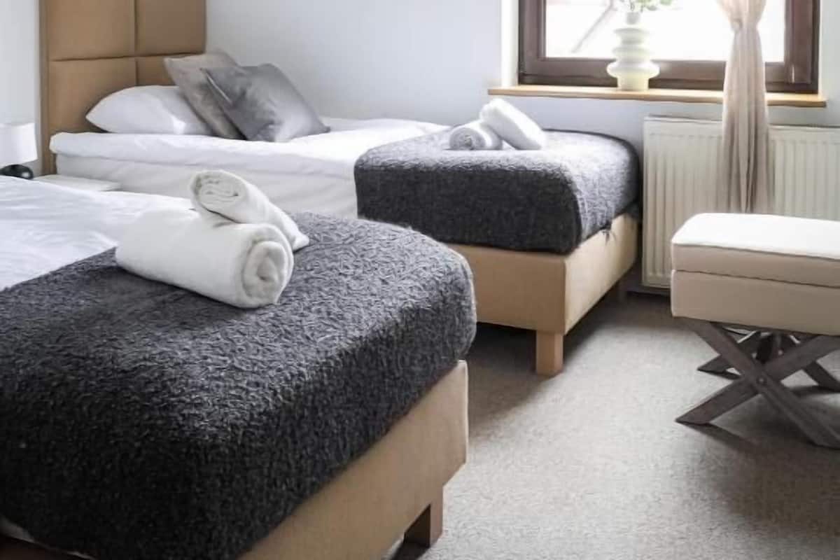 Ein Hotelzimmer mit zwei Betten, einem Fenster mit Vorhängen, einem Heizkörper und einem kleinen Tisch.