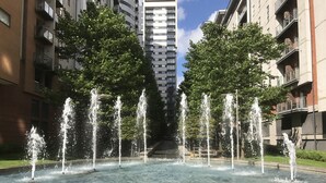 Ein öffentlicher Brunnen mit mehreren Wasserstrahlen in einem Innenhof, umgeben von Wohnhäusern.