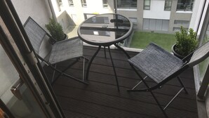 Ein Balkon mit einem Glastisch und vier Korbstühlen, der auf einen Innenhof mit Gebäuden im Hintergrund blickt.