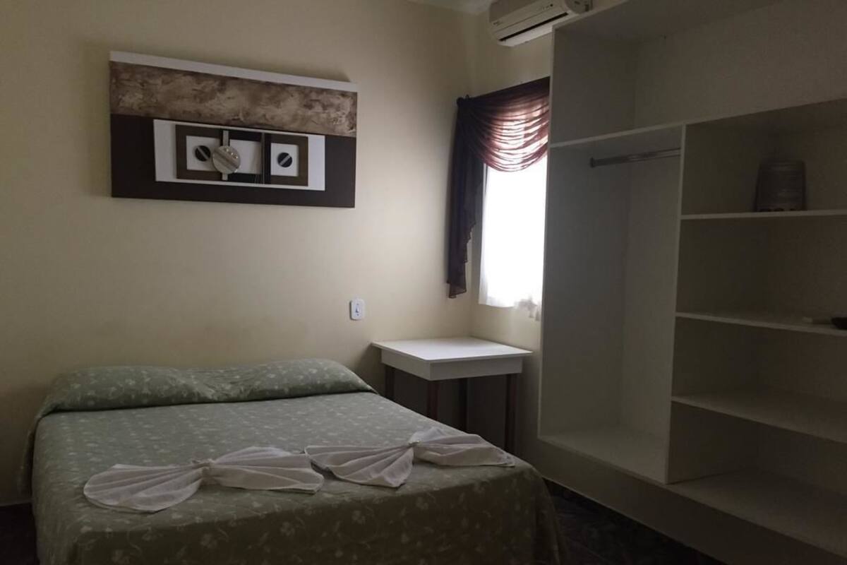 A hotel room with a bed, a small bedside table, a wardrobe, and a wall-mounted air conditioning unit.