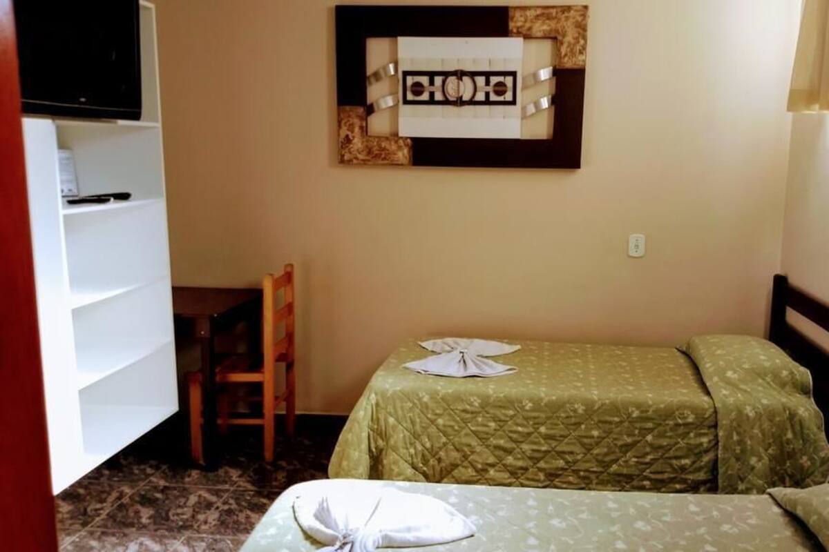 A small room with two beds, a TV on a shelf, and a wooden chair.