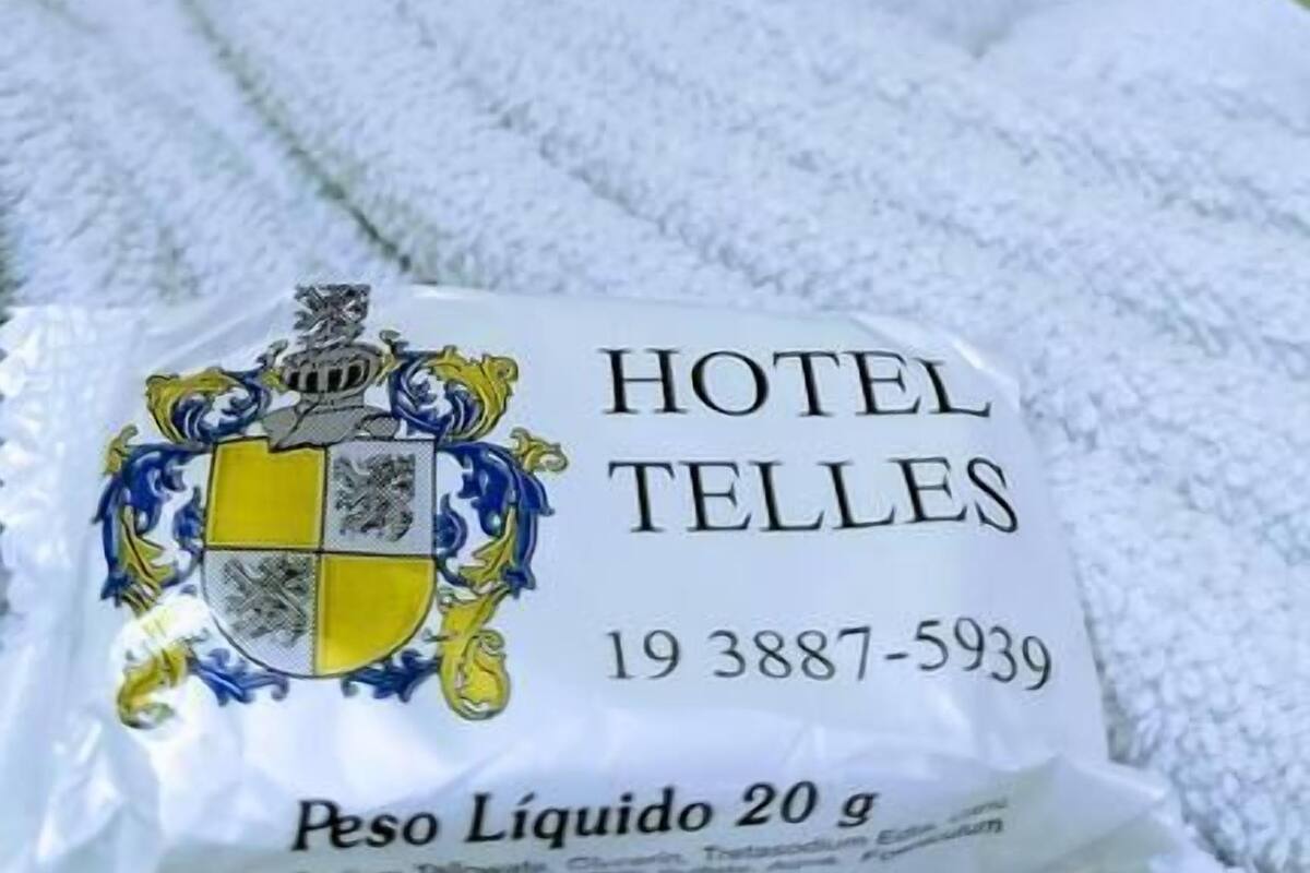 A white towel with a hotel emblem and contact number on a bed with a green pillow.