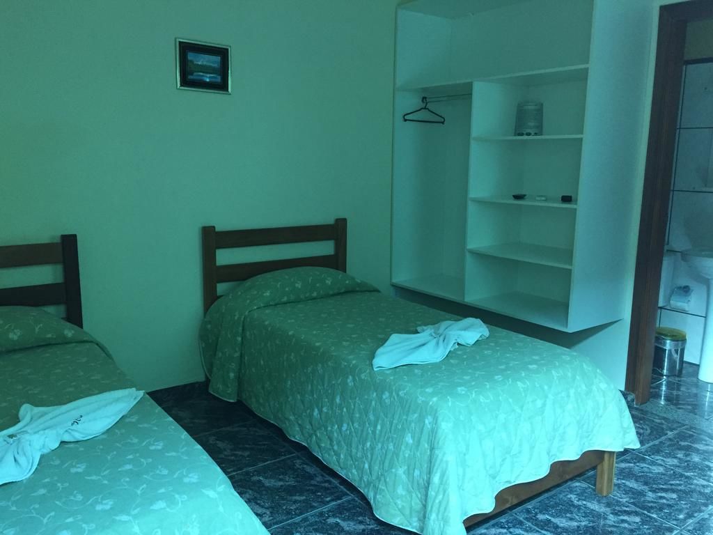 Quarto com duas camas, um guarda-roupa e uma pequena estante.