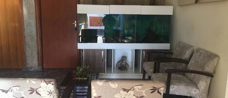 A room with a wooden door, a white cabinet with a fish tank, and two patterned armchairs.