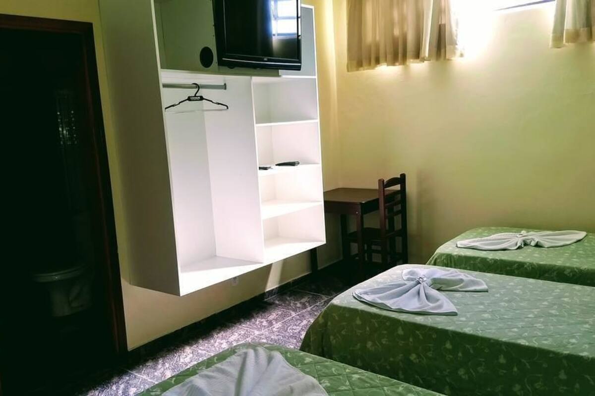 A hotel room with two beds, a TV mounted on a wall, a small table, and a wardrobe with shelves.
