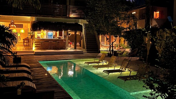 A pool area with lounge chairs, a bar, and a staircase leading to an upper level. - Pousada Raízes do Brasil (Porto Seguro)
