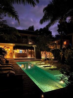 Un espace piscine comprenant des chaises longues, un bar et un escalier menant à un niveau supérieur.