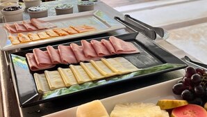 A buffet with various food items, including meats, cheeses, and fruits, set up outdoors with a view of palm trees and lounge chairs. - Pousada Raízes do Brasil (Porto Seguro)