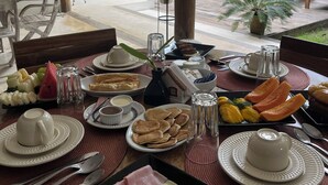 A dining table with various food items, plates, and utensils. - Pousada Raízes do Brasil (Porto Seguro)