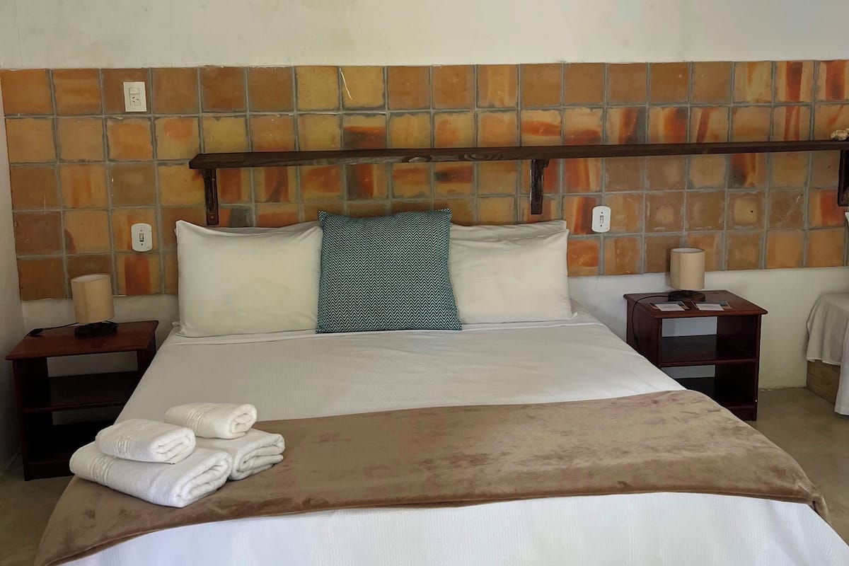 A hotel room with a tiled headboard, a bed with white bedding, two bedside tables with lamps, and a white rug.