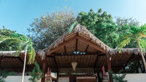 A thatched-roof structure with a wooden bench and a decorative hanging piece.