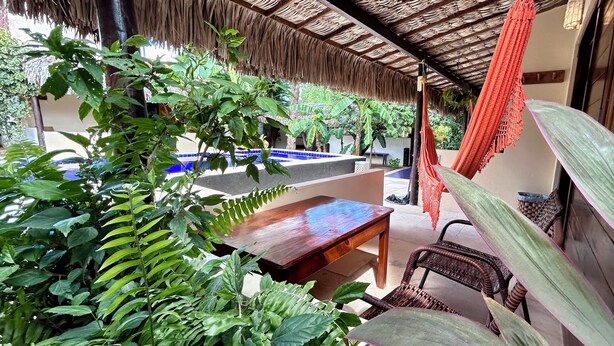 A covered outdoor area with a wooden bench, a hammock, and various plants.