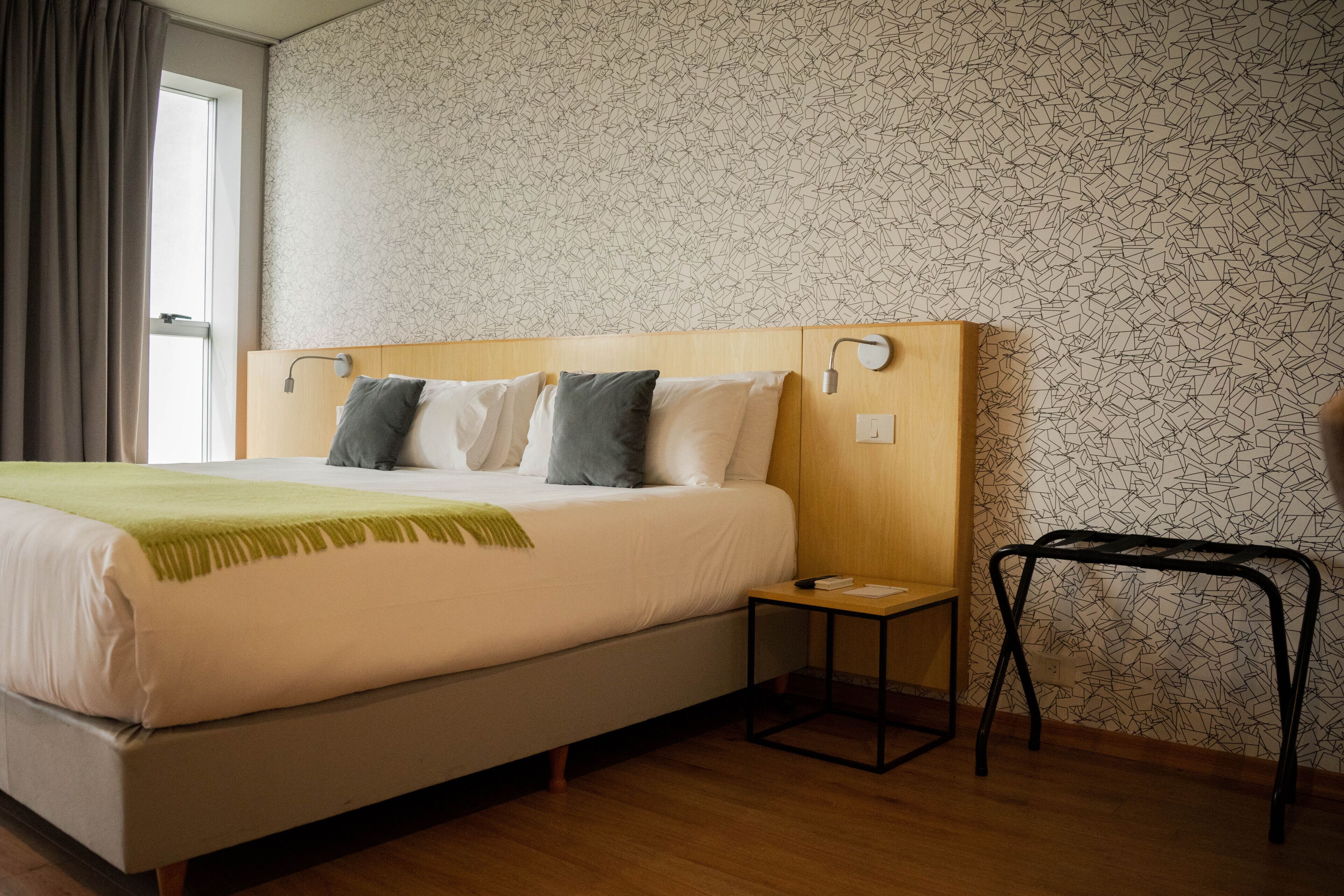 A neatly made bed with a green throw, a bedside table, and a small nightstand.