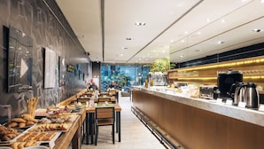 Un café moderno con una barra alargada, diferentes opciones de comida y asientos.