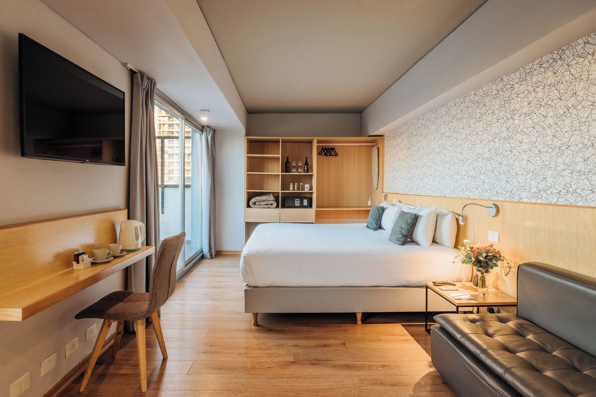 A modern hotel room with a bed, a desk, a chair, a sofa, and a TV.
