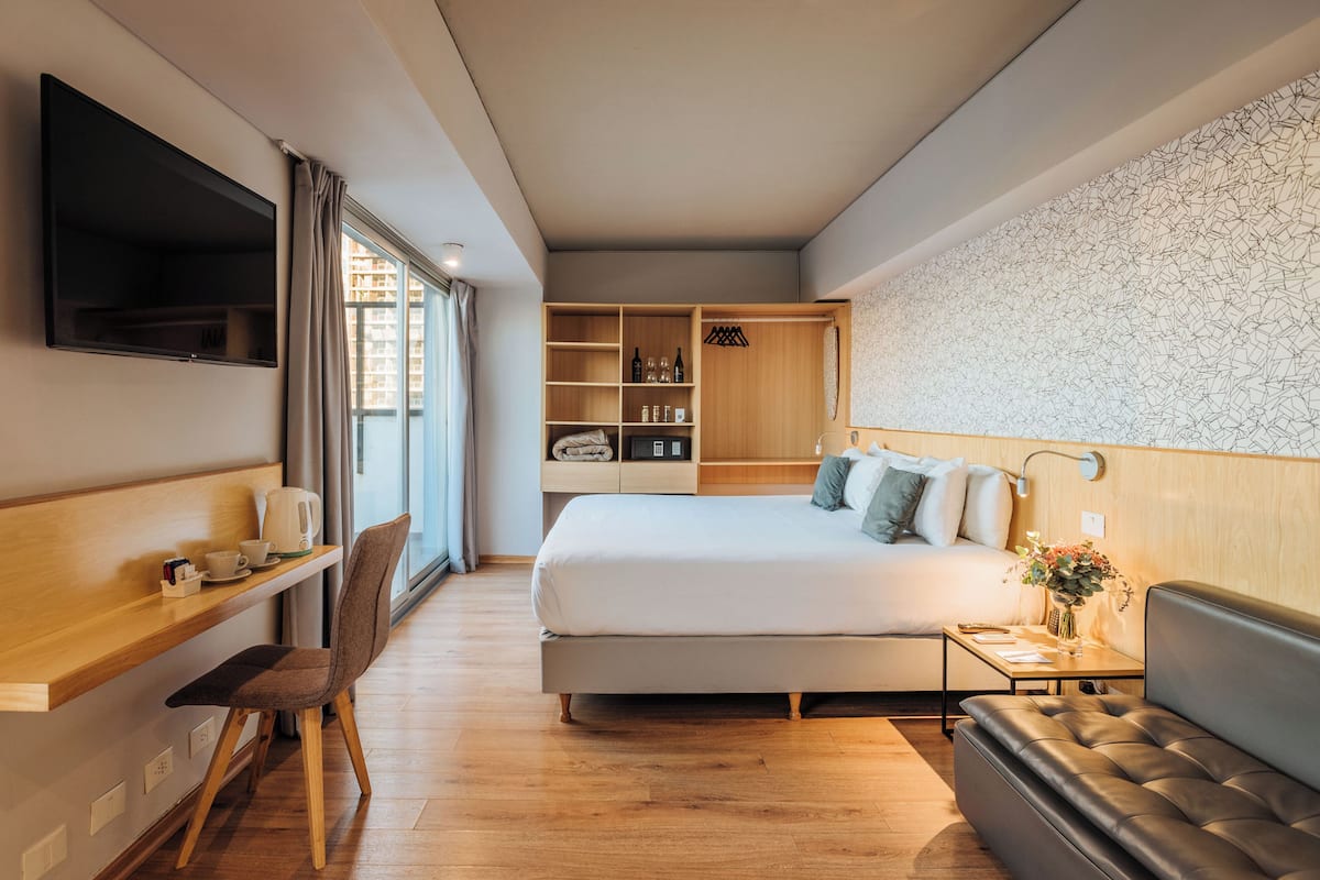 Una habitación de hotel moderna con cama, escritorio, silla, sofá y televisor.