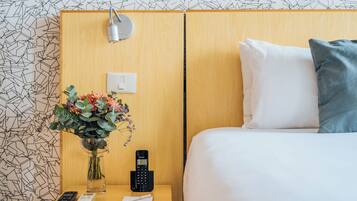 A hotel room with a wooden headboard, a bedside table with a vase of flowers, a remote control, a phone, and a pillow on the bed.