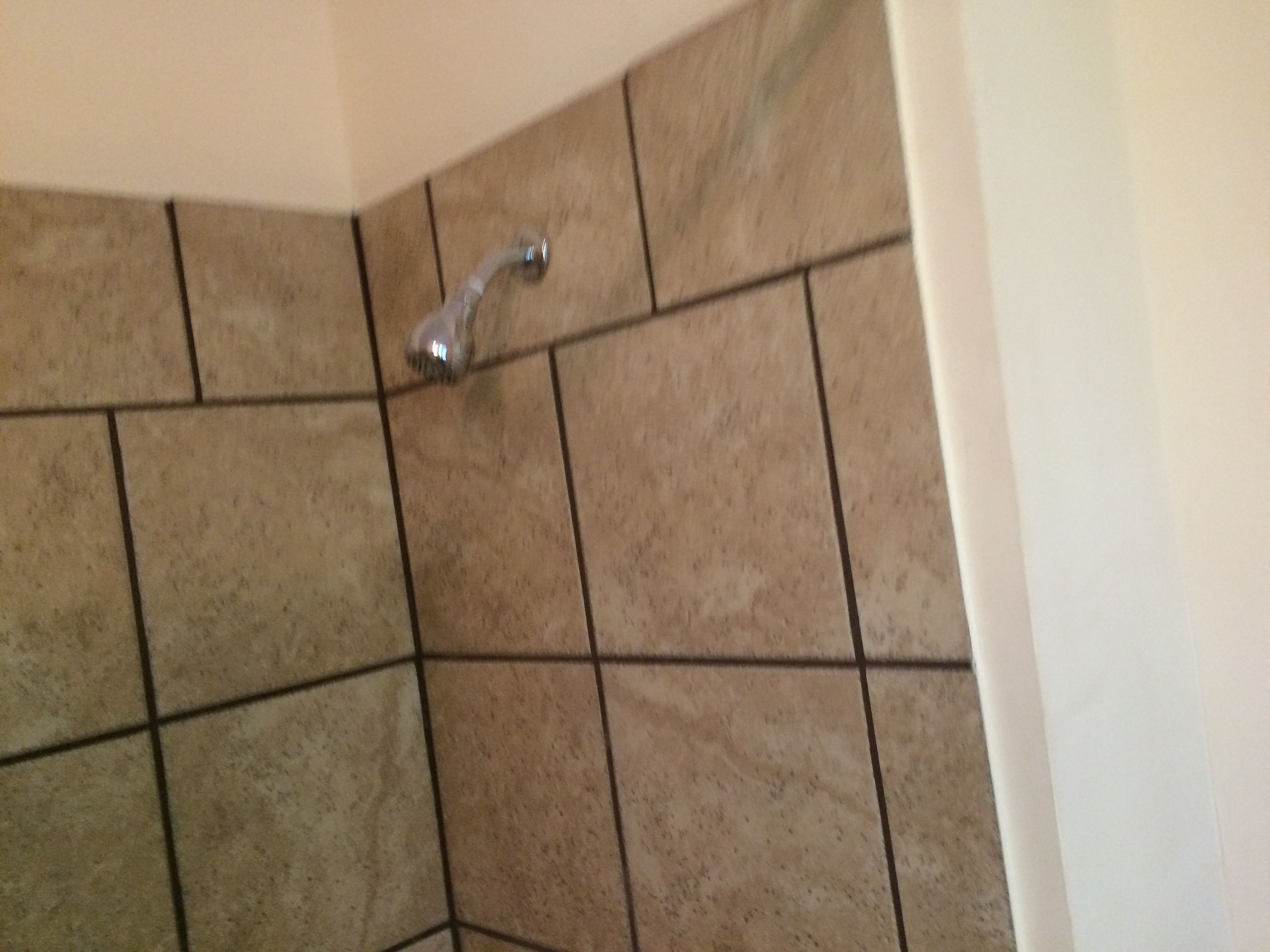 Esquina de un baño con azulejos color beige y un cabezal de ducha.