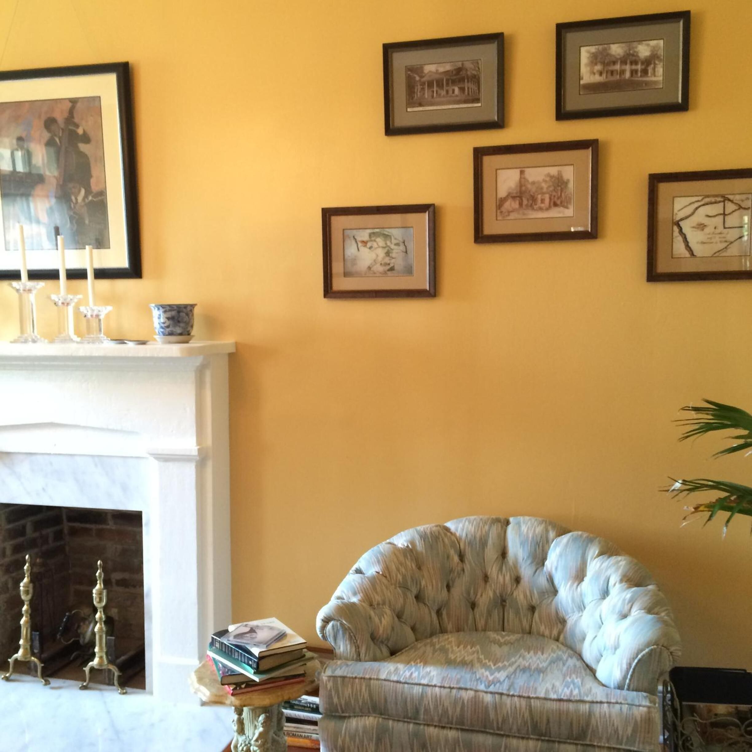 A living room with a fireplace, a white armchair, and several framed pictures on the wall.
