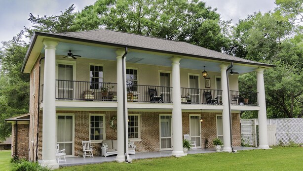 A two-story house with a covered porch, brick exterior, and white columns.