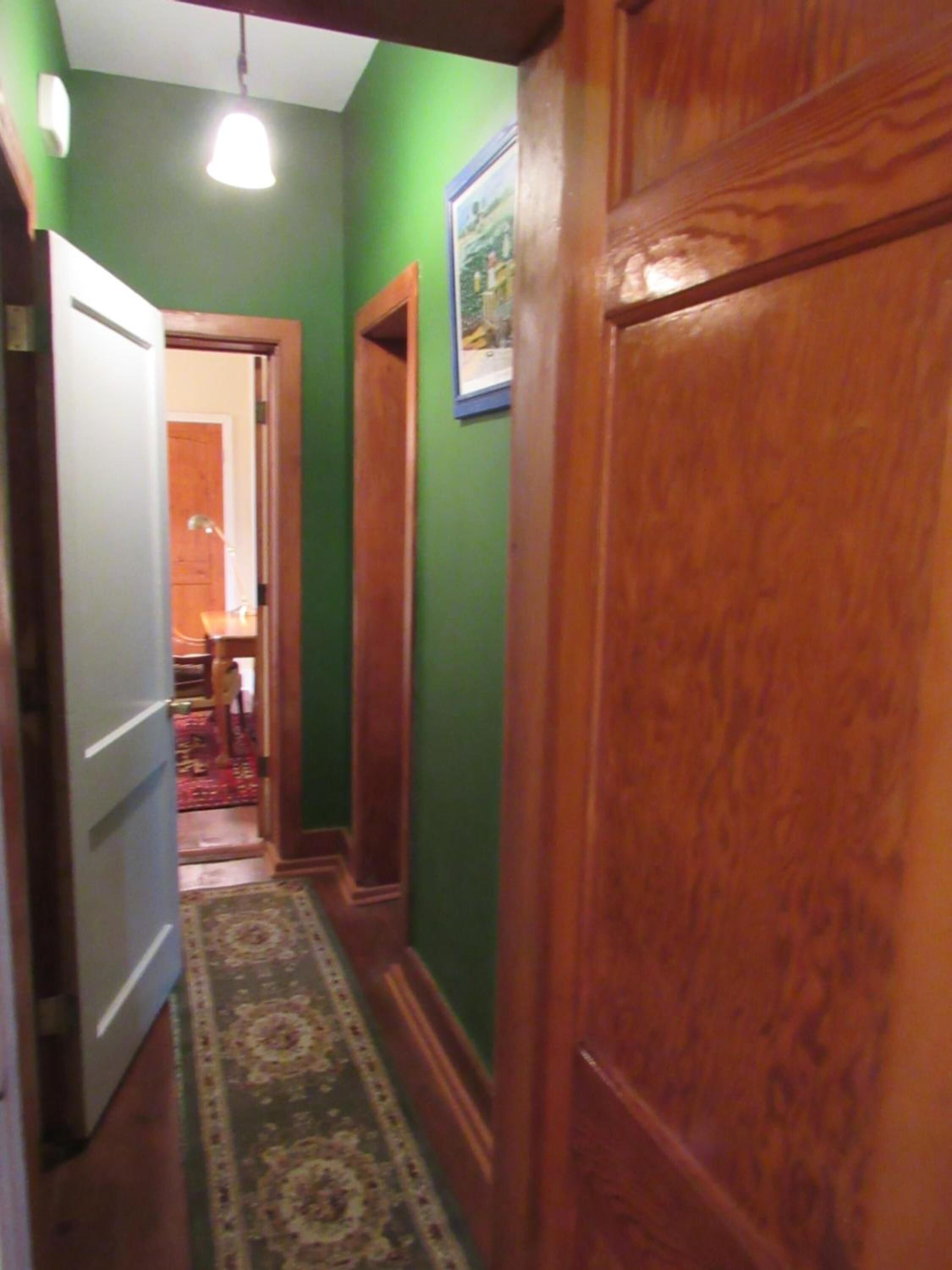 A narrow hallway with green walls, wooden doors, and a patterned carpet.