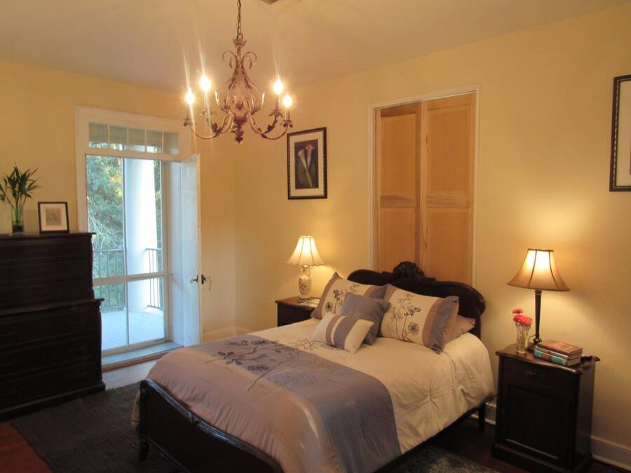 A bedroom with a bed, two bedside tables with lamps, a chandelier, a door, and a window.