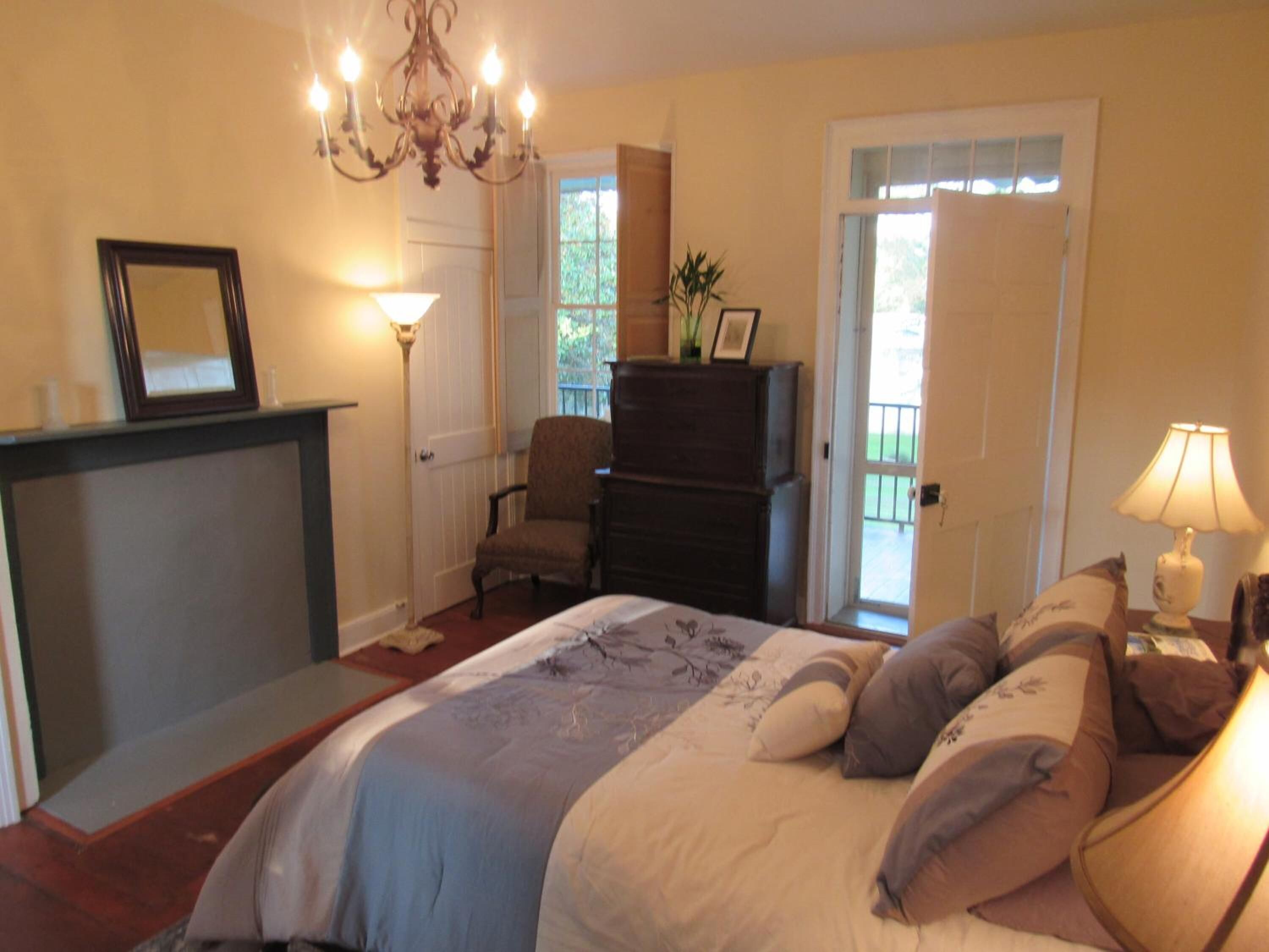 Un dormitorio con cama, cómoda, silla, escritorio, candelabro y puerta que da a un balcón.