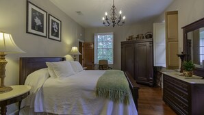 A bedroom with a large bed, a chandelier, a window, and a dresser.