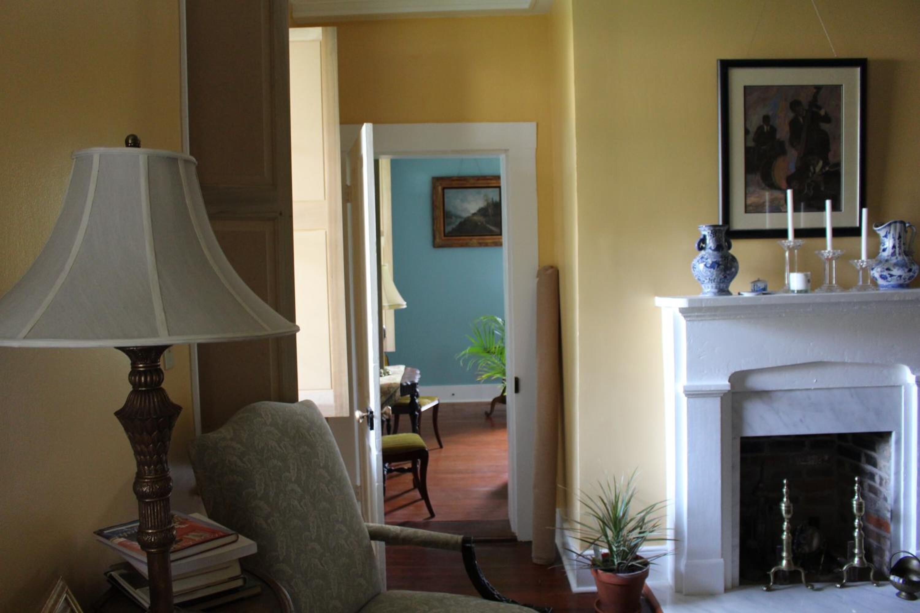 A room with a lamp, chair, books, a fireplace, and a painting on the wall.