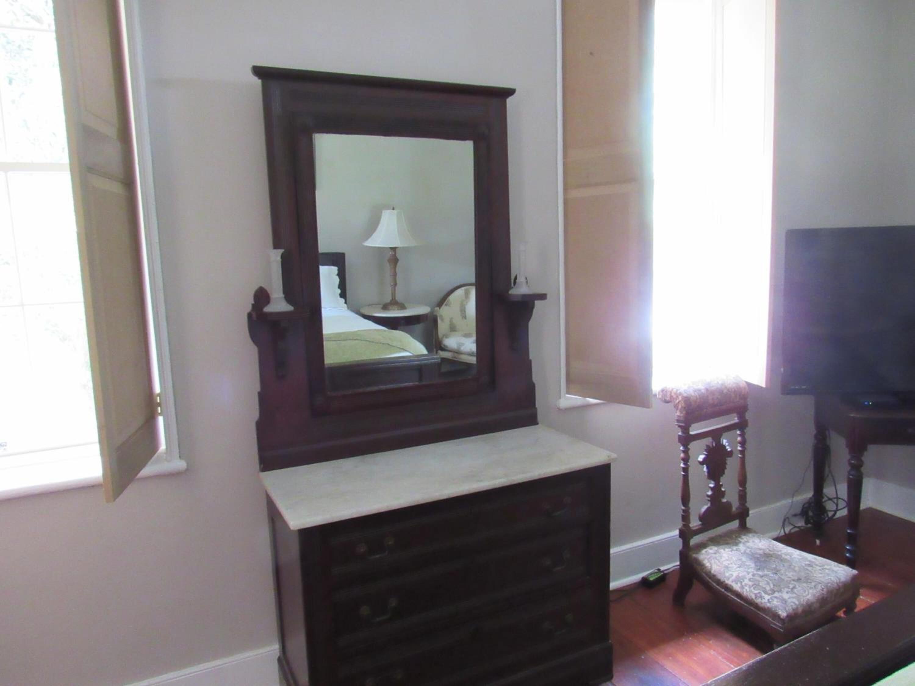 A room with a large mirror, a dresser, a chair, and a television.