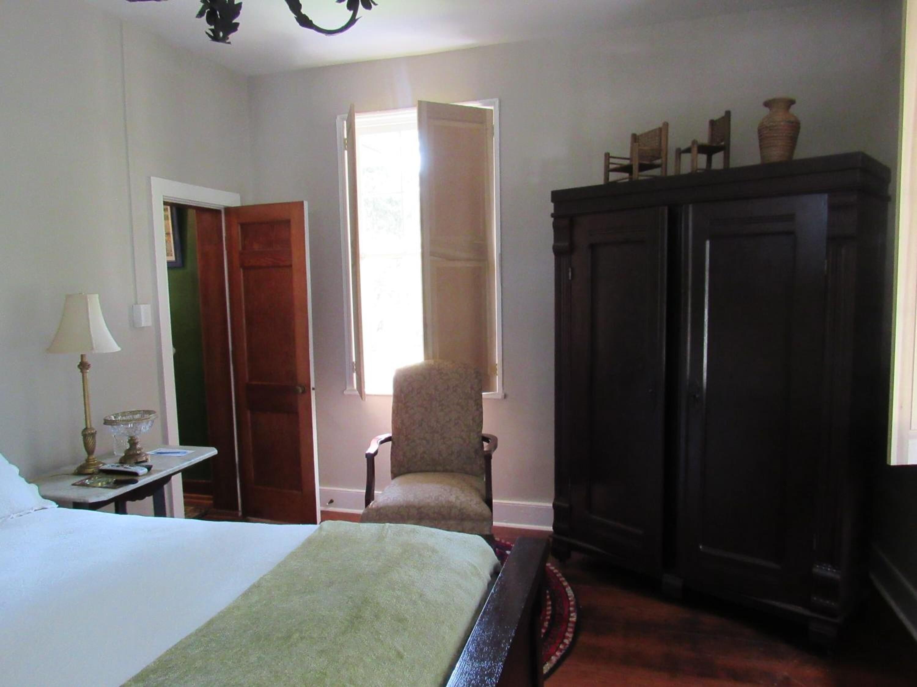 A bedroom with a bed, a chair, a wardrobe, and a window.