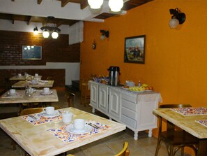 A dining area with tables set for service, a white bar counter with a coffee pot, and a painting on the wall. - Pousada Colina Verde (Garopaba)