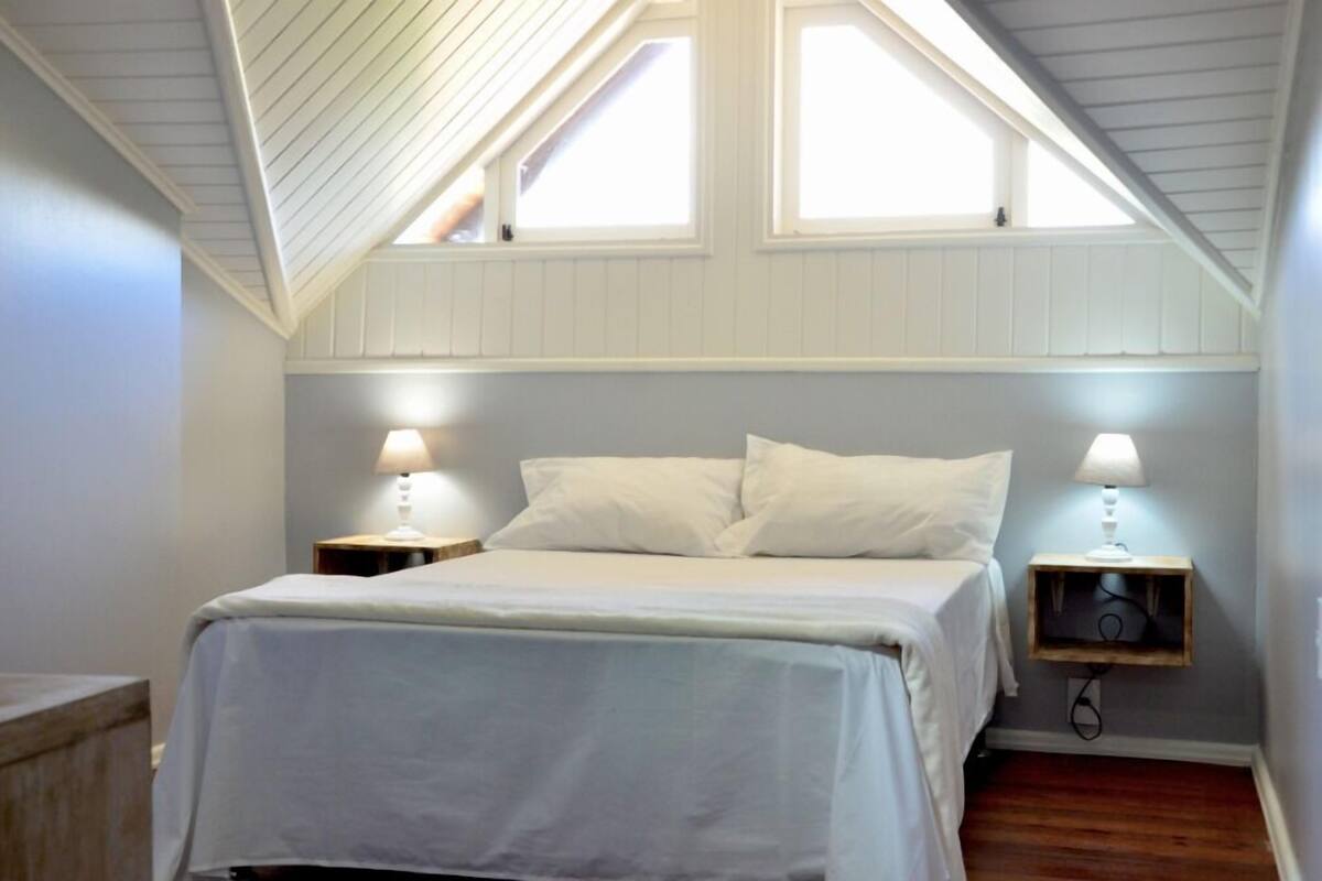 A bedroom with a sloped ceiling, two bedside lamps, a bed with white bedding, and a small wooden nightstand.