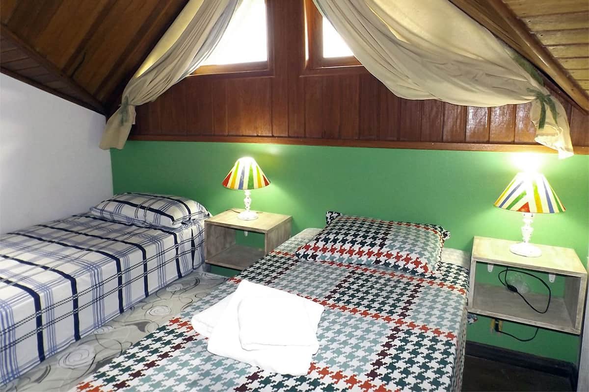 A dormitory room with two beds, each with a patterned bedspread, two bedside lamps, and a window with curtains.